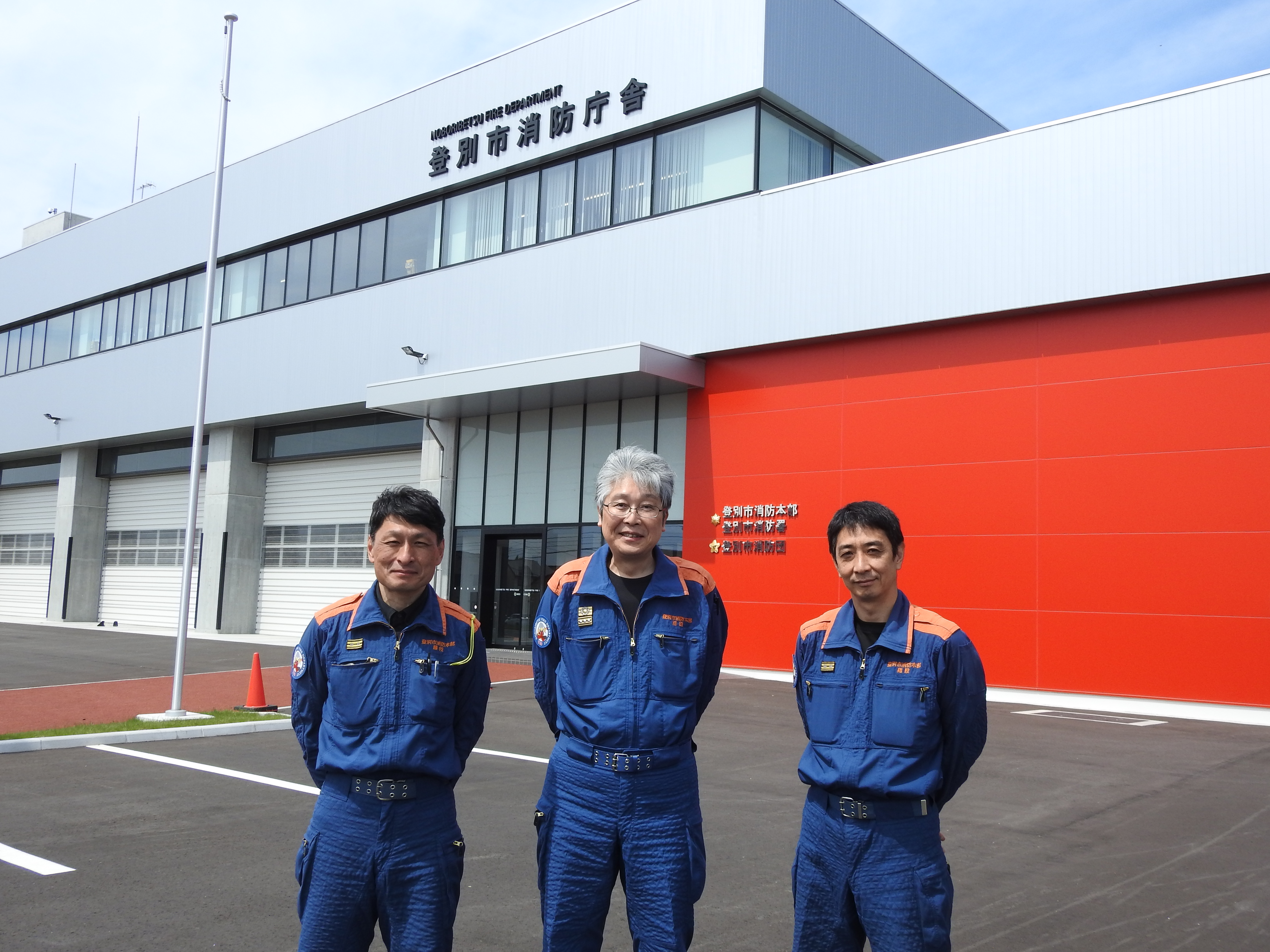パーソナリティ３人が消防庁舎の前で並んでいる写真です